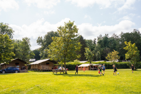 Bambini giocano a calcio in un campeggio erboso con tende e alberi a Camping de Chênefleur, Belgio.