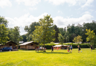 Bambini giocano a calcio in un campeggio erboso con tende e alberi a Camping de Chênefleur, Belgio.