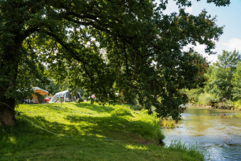Camping junto al río con tiendas y árboles en Chênefleur, Luxemburgo belga, escena soleada y tranquila.