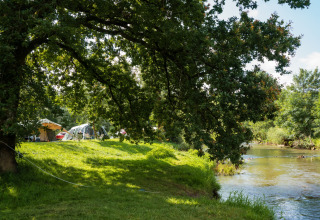 Camping au bord de la rivière avec tentes et arbres à Chênefleur, Luxembourg belge, scène paisible.
