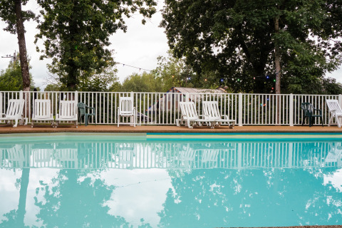 Piscina all'aperto con lettini e recinzione bianca, circondata da alberi al Camping de Chênefleur, Belgio.