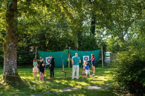 Niños y adultos disfrutan de tiro con arco bajo los árboles en Camping de Chênefleur, Luxemburgo, Bélgica.