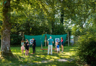 Børn og voksne deltager i bueskydning under træerne på Camping de Chênefleur, Luxembourg, Belgien.