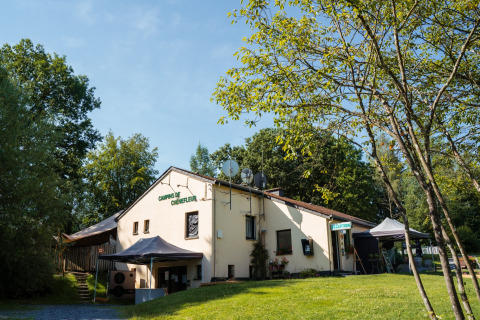 Reception building at Camping de Chênefleur holiday park, surrounded by trees in Luxembourg, Belgium.