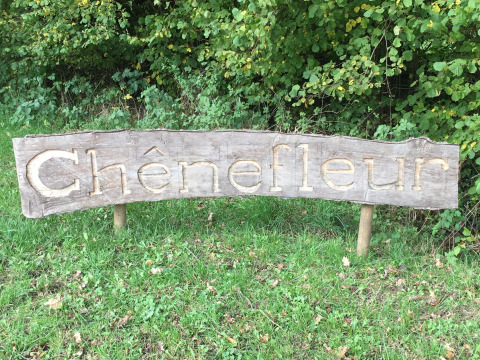 Cartello in legno con 'Chênefleur' davanti a cespugli al Camping de Chênefleur, Lussemburgo belga, Belgio.