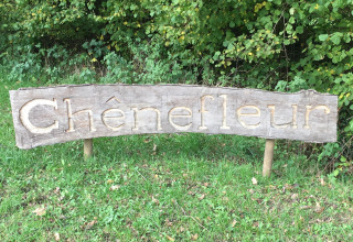 Cartello in legno con 'Chênefleur' davanti a cespugli al Camping de Chênefleur, Lussemburgo belga, Belgio.