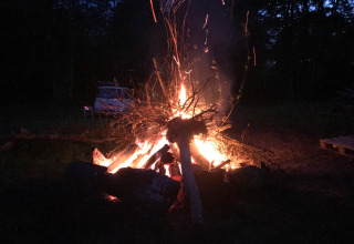 Een groot kampvuur brandt ’s avonds op Camping de Chênefleur, Luxemburg, België, met auto achteraan.