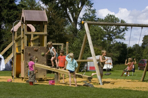 Bambini che giocano al parco giochi di Camping de Chênefleur in Lussemburgo, Belgio, circondati dal verde.