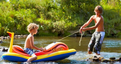Zwei Kinder spielen mit einem aufblasbaren Boot im Fluss bei Camping de Chênefleur in Belgien.