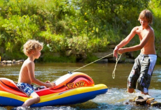 Due bambini giocano in un fiume con un gommone al Camping de Chênefleur, parco vacanze in Belgio.