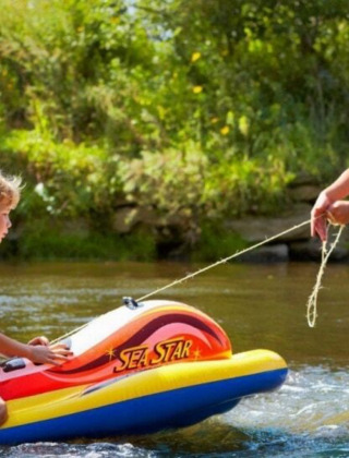 Zwei Kinder spielen mit einem aufblasbaren Boot im Fluss bei Camping de Chênefleur in Belgien.