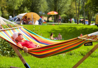 Een vrouw rust uit in een vrolijke hangmat op Camping de Chênefleur, Belgisch Luxemburg, omringd door tenten.