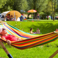 Una mujer descansa en una colorida hamaca en Camping de Chênefleur, Bélgica Luxemburgo, rodeada de tiendas y césped.