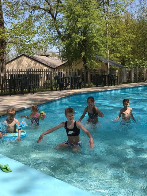 Bambini che giocano e schizzano nell’area piscina esterna di Camping de Chênefleur, Belgio, tra gli alberi.