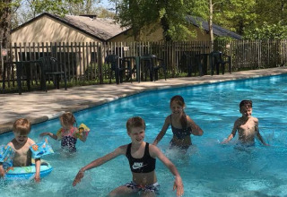 Bambini che giocano e schizzano nell’area piscina esterna di Camping de Chênefleur, Belgio, tra gli alberi.