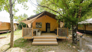 Vista exterior de una cabaña Villatent Outback en Medrose Camping, Francia, con terraza de madera entre árboles.