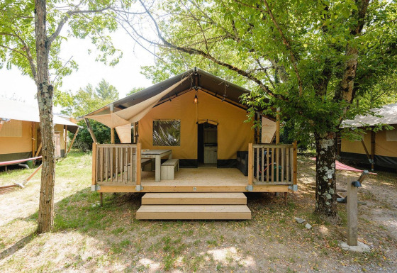 Vista exterior de una cabaña Villatent Outback en Medrose Camping, Francia, con terraza de madera entre árboles.