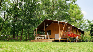 Tienda safari Villatent Nomad en Recreatiepark de Lucht, Países Bajos, rodeada de árboles y césped.