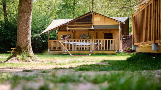 Tienda safari Villatent Ranger con hamaca sobre césped en Recreatiepark de Lucht, Países Bajos, rodeado de árboles