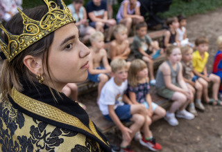 Een kind in koningkostuum treedt op voor een groep kinderen in Vakantiepark de Twee Bruggen, Gelderland.