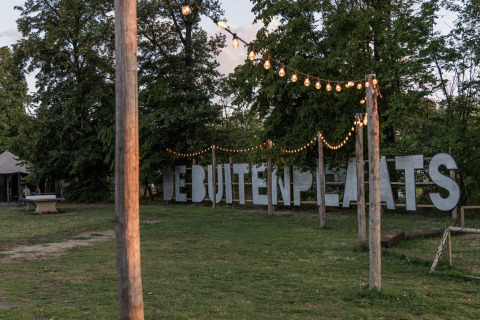 Outdoor area at Vakantiepark de Twee Bruggen, Gelderland, with string lights and large DEBUITENPLAATS sign.