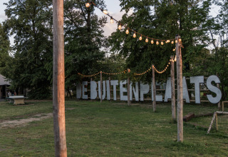 Buitenruimte in Vakantiepark de Twee Bruggen, Gelderland, met lichtsnoeren en groot DEBUITENPLAATS-bord.