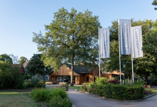 Ingang van Vakantiepark de Twee Bruggen in Gelderland, Nederland, met vlaggen, bomen en tuin.