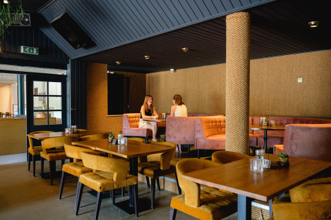 Interior moderno de cafetería con asientos acolchados y mesas de madera en Vakantiepark de Twee Bruggen, Gelderland, Países Bajos.