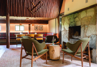 Hyggelig lounge ved pejsen i Vakantiepark de Twee Bruggen, Gelderland, med vintage stole og træborde.