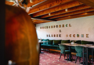 Modern restaurant interior with green velvet chairs, wooden ceiling, and 'BOERENDUMMEL & BLANKE DEERNE' on wall.