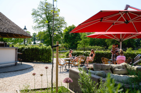 Zona de terraza exterior con sombrillas rojas y visitantes relajándose en Vakantiepark de Twee Bruggen, Países Bajos.