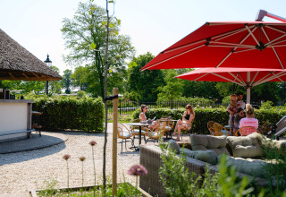 Zona de terraza exterior con sombrillas rojas y visitantes relajándose en Vakantiepark de Twee Bruggen, Países Bajos.