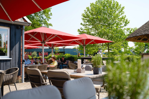 Terraza exterior con sombrillas rojas y huéspedes en Vakantiepark de Twee Bruggen, Gelderland, Países Bajos.