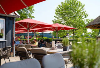 Buitenterras met rode parasols en bezoekers in Vakantiepark de Twee Bruggen, Gelderland, Nederland.