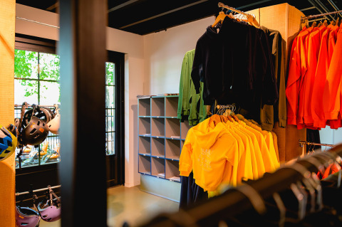 En el interior de una tienda en Vakantiepark de Twee Bruggen con sudaderas y cascos coloridos exhibidos.