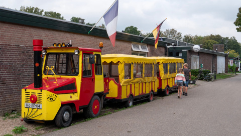 Klein, kleurrijk treintje bij Camping de Krabbeplaat vakantiepark, twee kinderen lopen erlangs.