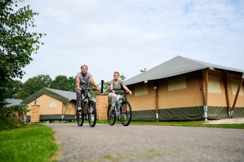 Dos personas montan bicicletas junto a tiendas de lujo en Vakantiepark Sallandshoeve, Overijssel, Países Bajos.