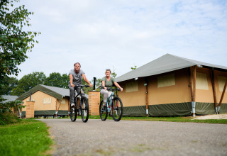 Twee personen fietsen langs lodgetenten in Vakantiepark Sallandshoeve, Overijssel, Nederland.