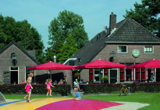 Kinderen spelen in een kleurrijke speeltuin bij een gebouw met rode parasols in Vakantiepark Sallandshoeve.