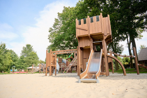 Parque infantil con estructura de madera y tobogán sobre arena en Vakantiepark Sallandshoeve, Países Bajos.