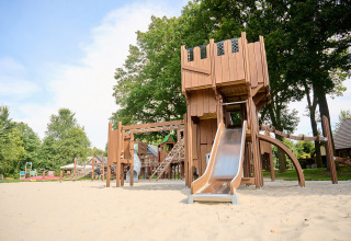 Houten speeltuin met glijbaan op zand in Vakantiepark Sallandshoeve, omgeven door bomen en groen.