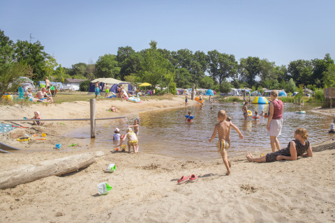Familias y niños juegan junto al lago en Vakantiepark Sallandshoeve, rodeados de tiendas y vegetación.