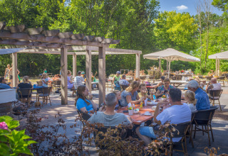 Buitencafé bij Vakantiepark Sallandshoeve, Overijssel, met mensen onder pergola’s in groene omgeving.