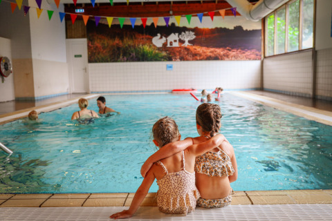 Dos niños pequeños sentados juntos junto a la piscina cubierta en Vakantiepark Sallandshoeve, Overijssel, Países Bajos.