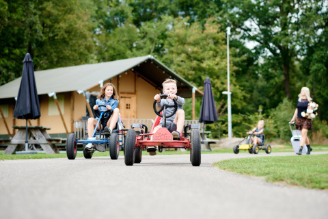 Niños montan en karts frente a tiendas lodge en Vakantiepark Sallandshoeve, Overijssel, Países Bajos.