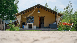 Tienda safari Villatent Nomad en Vakantiepark Sallandshoeve, Países Bajos, con hamaca y terraza exterior.