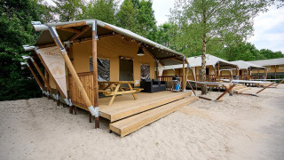 Tienda tipo safari Villatent Cottage en Vakantiepark Sallandshoeve, Países Bajos, rodeada de arena y árboles.