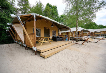 Tienda tipo safari Villatent Cottage en Vakantiepark Sallandshoeve, Países Bajos, rodeada de arena y árboles.