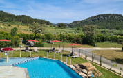 Swimmingpool med liggestole, røde parasoller og udsigt over grønne bakker på Camping De l'Olivigne i Occitanie.