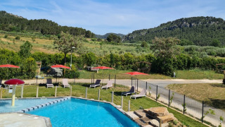 Piscina all'aperto con lettini e ombrelloni rossi circondata da colline verdi al Camping De l'Olivigne, Occitanie.